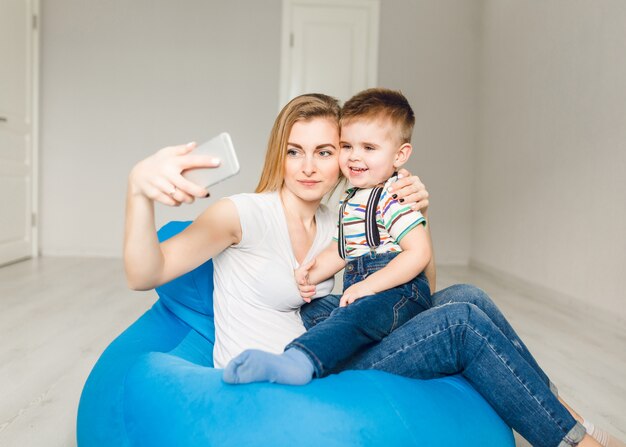 Studio shot of a mother holding her child and taking a selfie on smartphone.