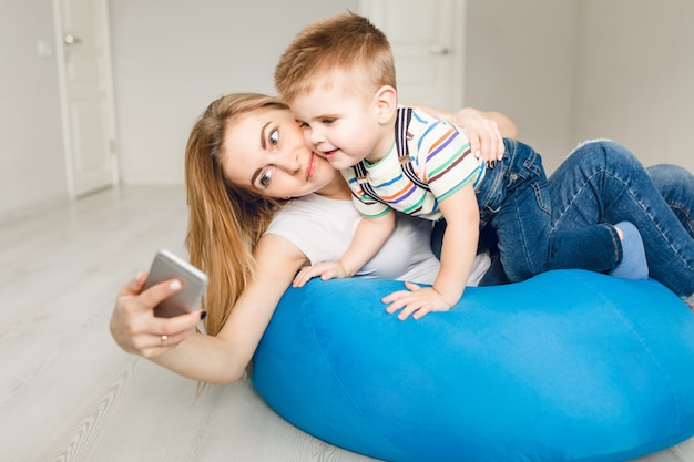 スマートフォンで彼女の子供を保持し、selfieを取る母のスタジオ撮影