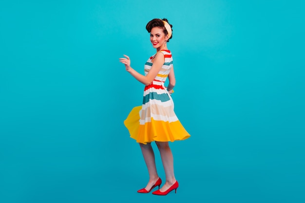 Studio shot of pinup girl wearing striped dress. Full length view of dancing stylish woman.