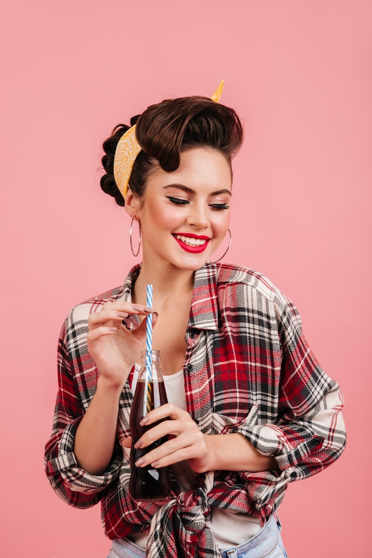 Free Photo studio shot of pinup lady isolated on pink background. laughing girl in checkered shirt drinking soda.