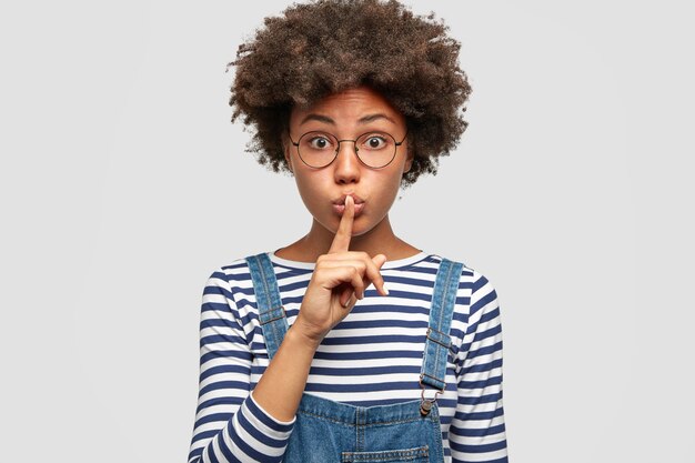 Studio shot of pleasant looking mysterious young female shows hush gesture