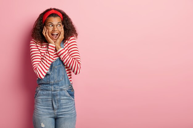 Studio shot of pleasant teenage girl posing in overalls with curly hair