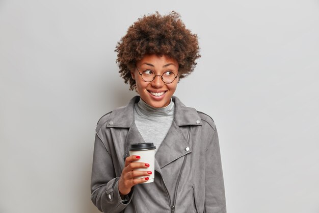Studio shot of pleased smiling Afro American woman holds paper cup of coffee