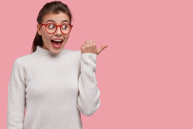 Foto gratuita studio shot di positivo giovane felice ride e punti a parte, mostra qualcosa di incredibile, vestito con abiti casual