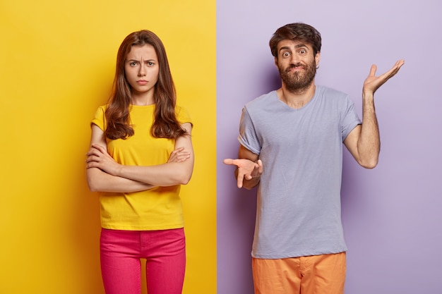 Studio shot of puzzled millennial couple posing against the dual colored wall