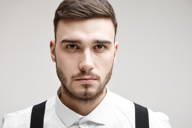 Studio shot of serious young unshaven Caucasian male entrepreneur staring at camera with deep in thoughts look, thinking over some business problem. People, modern lifestyle, job and career concept