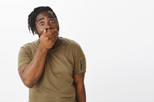 Studio shot of shocked guy in a brown t-shirt posing against the white wall