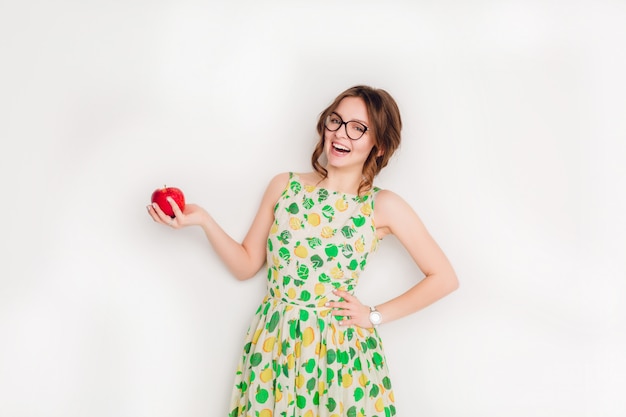 広く笑っている笑顔のブルネットの少女のスタジオ撮影。彼女は右手に赤いリンゴを持っています