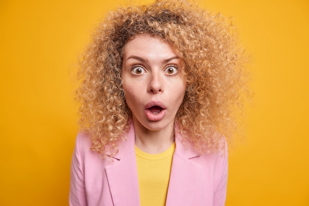 Free photo studio shot of startled young woman with curly bushy hair stares at camera