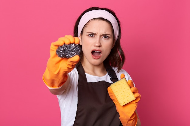 Studio shot of stressed sad woman standing isolated over pink wall with dirty sponge