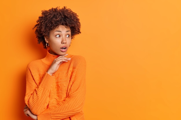 Studio shot of stupefied African American woman holds chin and stares aside