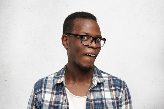 Studio shot of stylish African male in glasses staring at camera, having crazy look