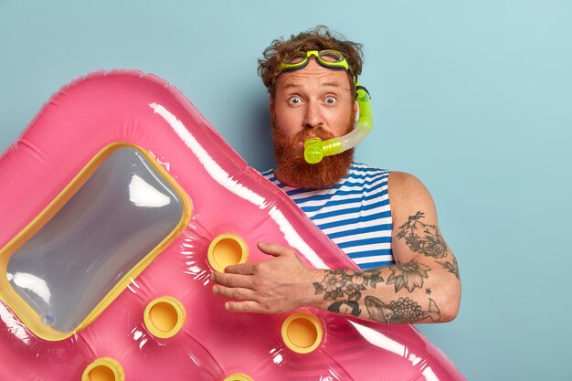 Studio shot of surprised bearded red man wears snorkel mask