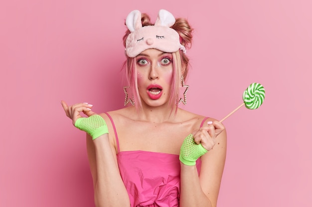 Studio shot of surprised blonde young woman with vivid makeup keeps mouth opened