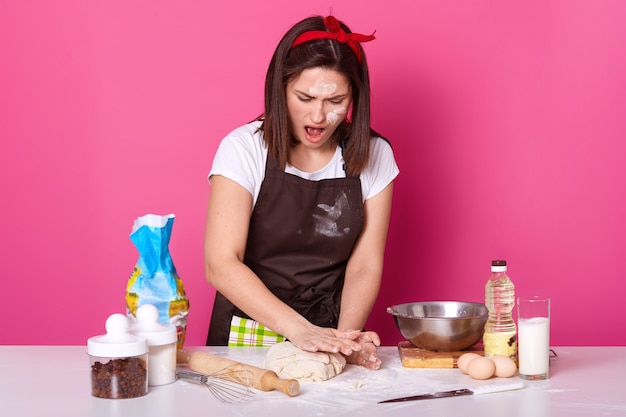 Studio shot of surprised woman wearing white t shirt and dirty apron with flour