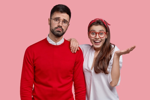 Studio shot of upset bearded man feels apathy, dissatified with everything, his female companion tries to cheer up, raises palm