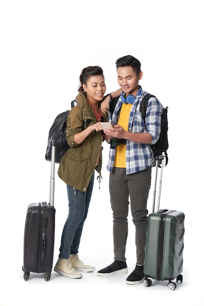 Studio shot of young couple with baggage surfing the net on smartphone