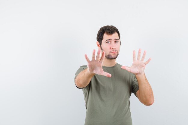 Studio shot of young handsome guy in khaki t-shirt open and extends hands to camera and showing i am not guilty gesture isolated on white background