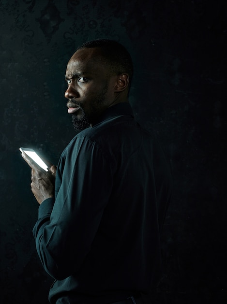 Studio shot di giovane serio africano nero uomo pensare mentre si parla al telefono cellulare su sfondo nero studio