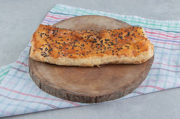 Stuffed pastry with sesame seeds on wood piece. 