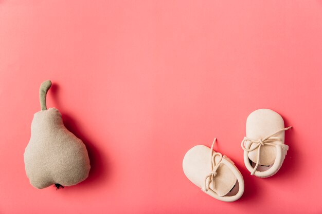 stuffed pear fruit and pair of baby's shoes on colored background
