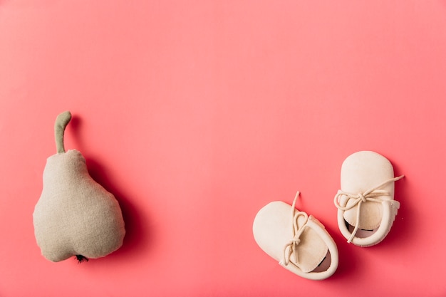 Stuffed pear fruit and pair of baby's shoes on colored background