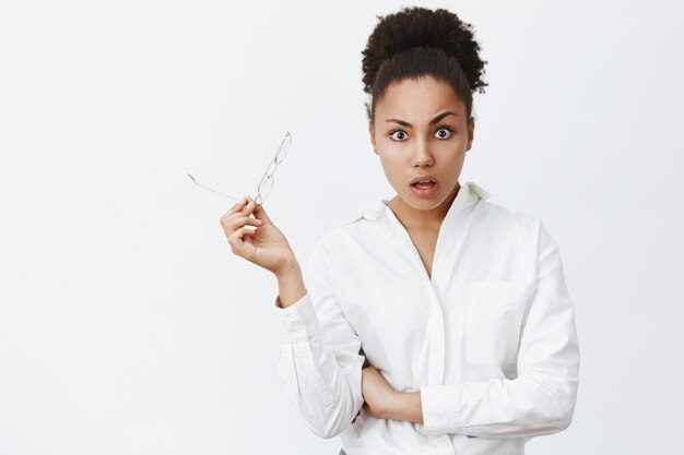 Stunned and amazed good-looking dark-skinned female woman in white shirt, taking of glasses from surprise and shock