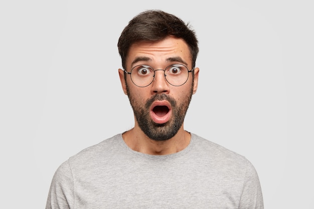 Free photo stunned emotive bearded man keeps mouth widely opened, looks with bated breath