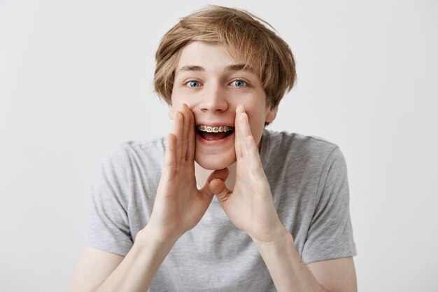 Stunned overjoyed caucasian male student screams with excitement, keeps hands near mouth, being glad to enter university or college. Emotional happy surprised young fair-haired man yells wow or omg
