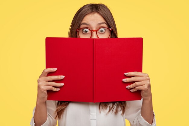 Stunned young brunette with glasses posing against the yellow wall