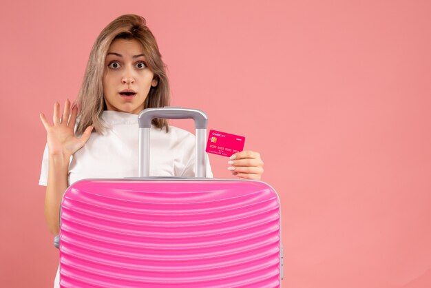 stunned young woman with pink suitcase holding card