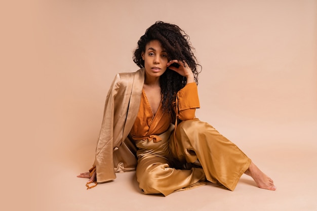 Stunning  african model with voluminous curly hairstyle in elegant   costume posing  on beige wall.