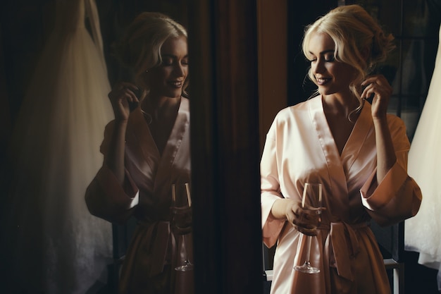 Stunning blonde lady in silk robe stands with glass of champagne