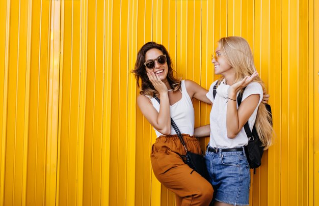 Stunning brown-haired woman in glasses laughing with blonde friend.