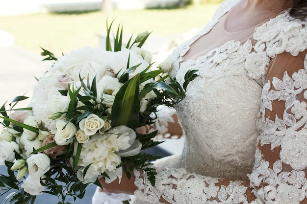 Stunning brunette bride holds rich white wedding bouquet