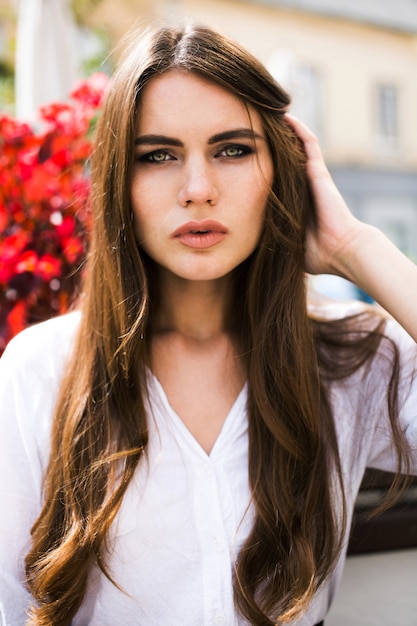 Stunning brunette with long hair sits before red flowers