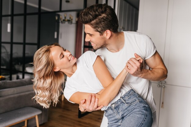 Stunning caucasian girl looking at boyfriend with smile. Indoor portrait of spectacular young woman dancing with husband.