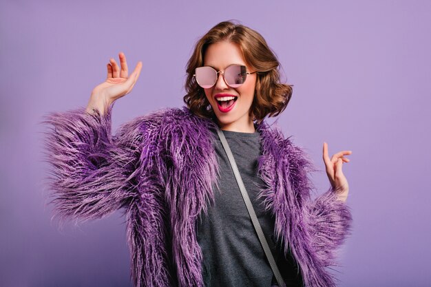 Stunning cute girl with curly brown hair posing with pleasure on purple background