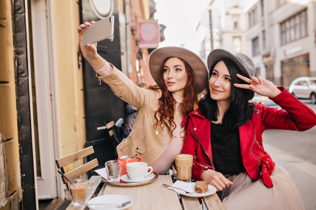 Splendida donna dai capelli scuri in giacca rossa che gode del dessert in un caffè all'aperto, che riposa con il migliore amico