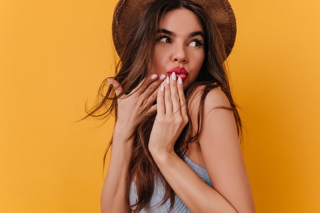 Stunning european girl in trendy hat covering mouth with hand and looking away