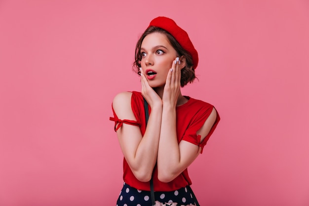 Stunning european woman in red outfit looking around with mouth open. Indoor photo of spectacular french girl with short hair.