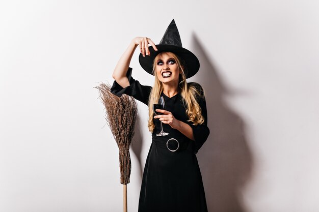 Потрясающая злая ведьма с метлой. Эффектная женщина с темным макияжем на Хэллоуин, корча рожи.
