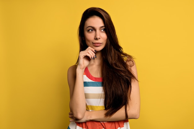 Stunning female model posing with face expression. Close-up portrait of stylish european girl standing with playful look in front of wall