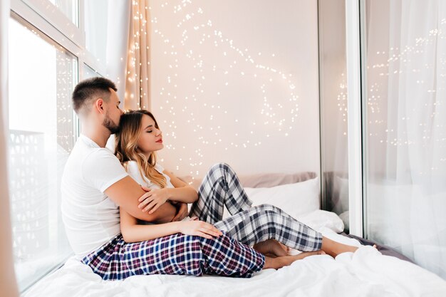 彼氏とポーズをとって怠惰なパジャマ姿の見事な女の子。週末に夫の近くのベッドに横たわっている愛らしい若い女性。