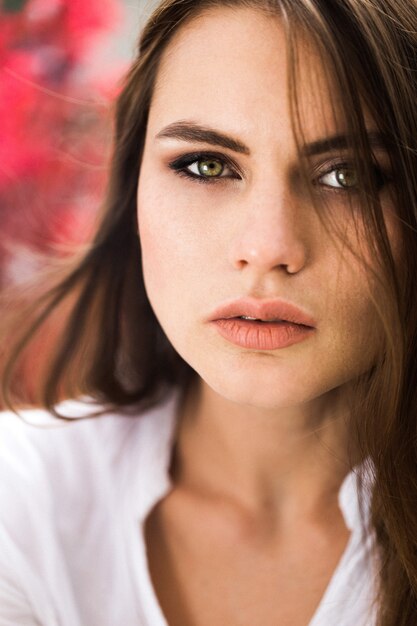 Stunning green-eyed woman sits before red flowers