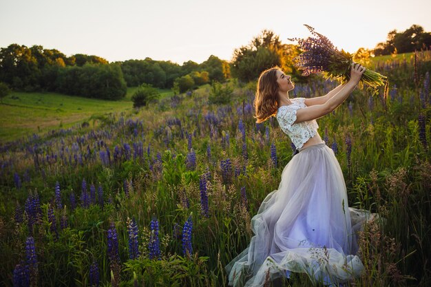 Stunning lady in white dress stands with bouquet on the field 