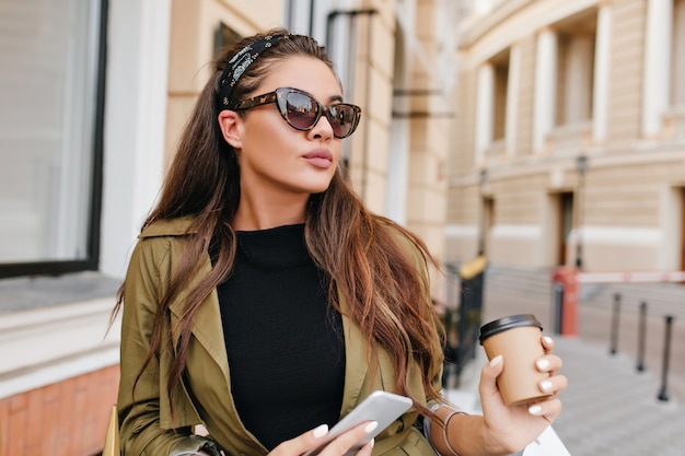 Stunning latin female model with nude make-up holding cup of coffee and walking down the street