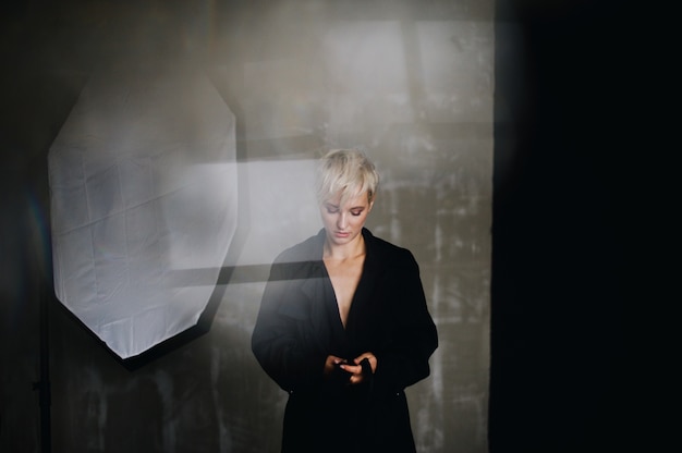 Stunning model with short white hair poses in black coat before a soft-box