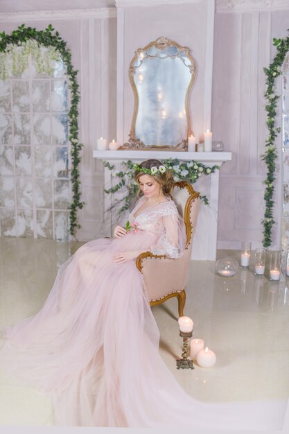 핑크 드레스에 멋진 임신 한 여자는 반짝 촛불으로 둘러싸인 소파에 달려