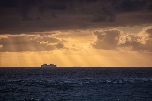 日没時に曇り空の下で穏やかな青い海と船のシルエットの見事なショット